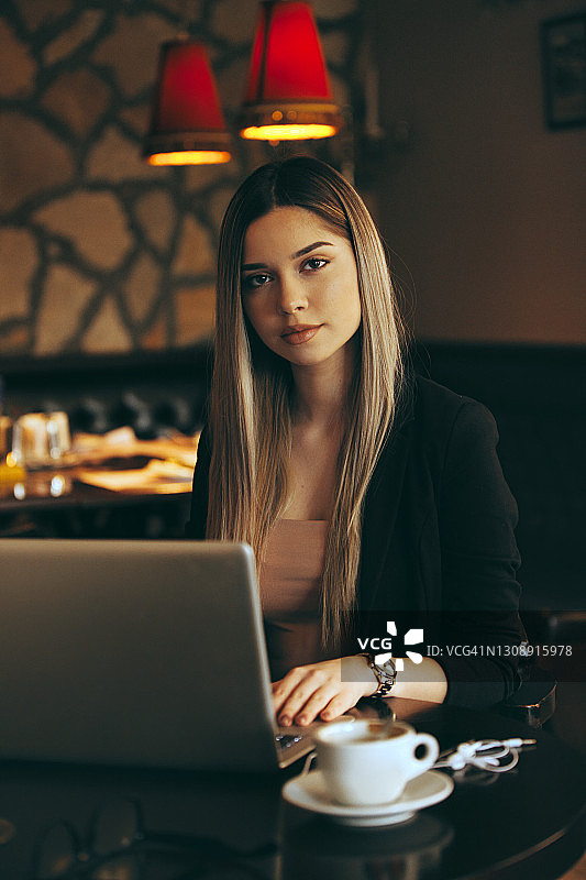 年轻女人在咖啡店一边喝咖啡一边用笔记本电脑工作图片素材