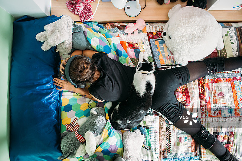 戴着耳机看设备，背上睡着猫的青少年女孩图片素材