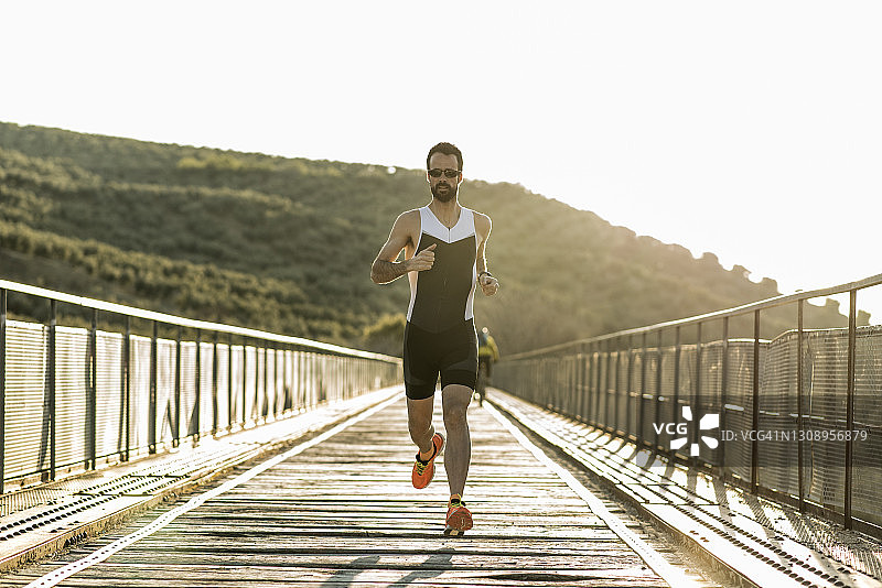 在桥上日落时训练的铁人三项运动员全身像图片素材