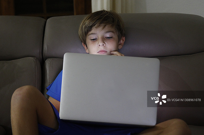 在黑暗中看笔记本电脑的男孩图片素材