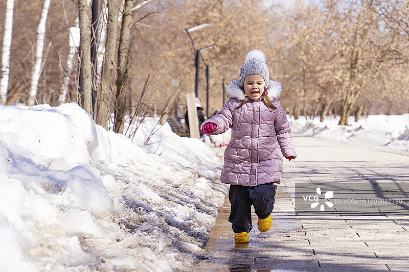 穿着黄色雨靴在春天水坑里跳跃的小白人女孩图片素材