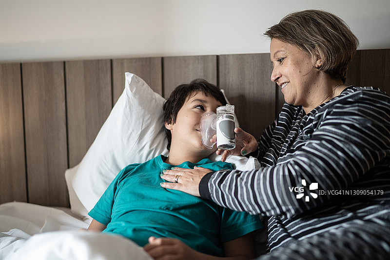 母亲帮助儿子使用雾化器进行吸入治疗图片素材