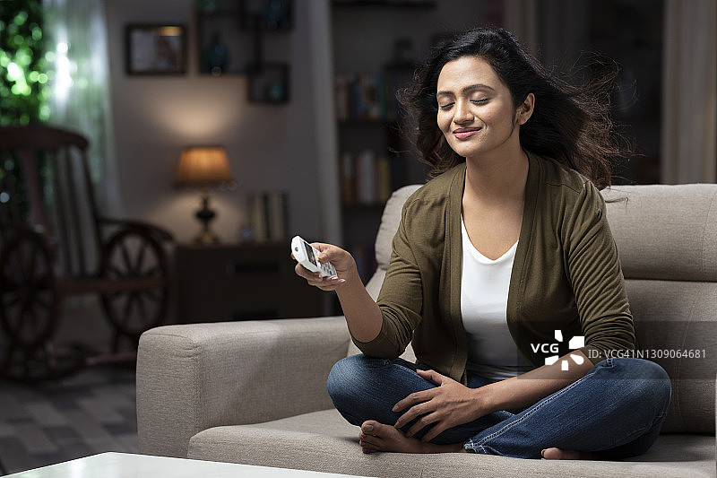 年轻女人坐在沙发上打开空调图片素材