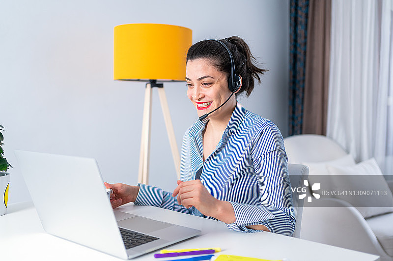 在家居办公室进行视频通话的微笑年轻女人，远程工作，在呼叫中心工作的女人图片素材