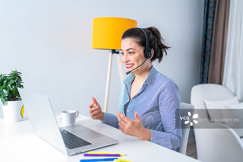 在家居办公室进行视频通话的微笑年轻女人，远程工作，在呼叫中心工作的女人图片素材