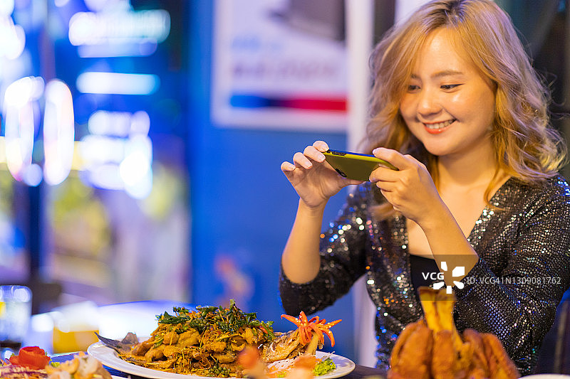 快乐的亚洲女性在餐厅用智能手机拍摄她的晚餐图片素材