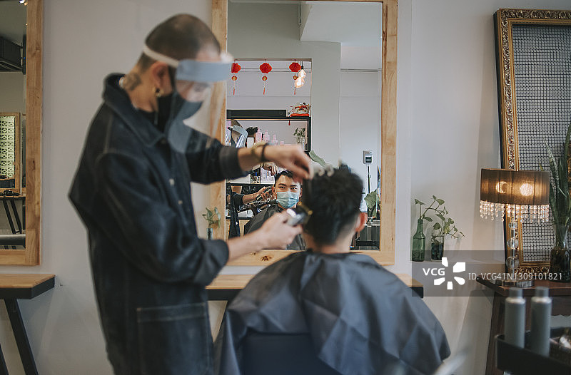 发廊里，亚裔发型师戴着防护服为顾客理发图片素材