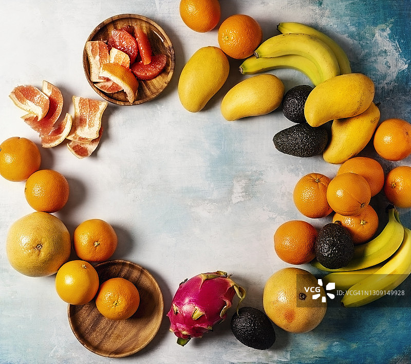 蓝色背景上的各种热带水果（香蕉、橙子、葡萄柚、芒果、鳄梨和火龙果）图片素材
