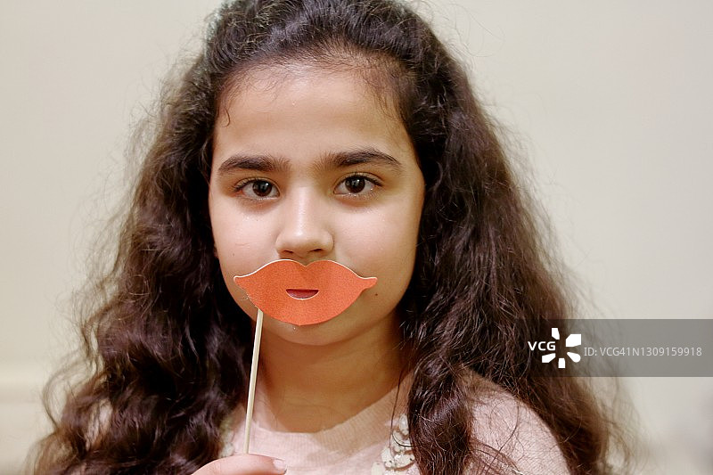 一名年轻女孩拿着粉色嘴唇道具对着镜头微笑图片素材