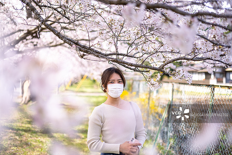 在樱花树下戴防护面罩的年轻女子肖像图片素材
