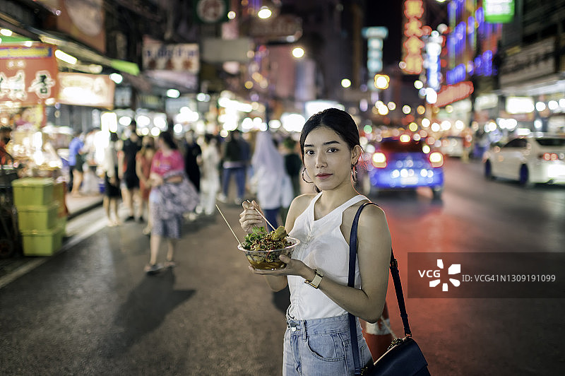 在泰国曼谷唐人街吃烤鱿鱼的年轻女人图片素材
