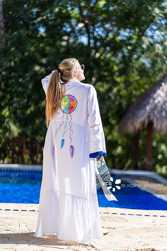 竖版照片：穿着白色民族风睡袍的金发女子在游泳池前图片素材