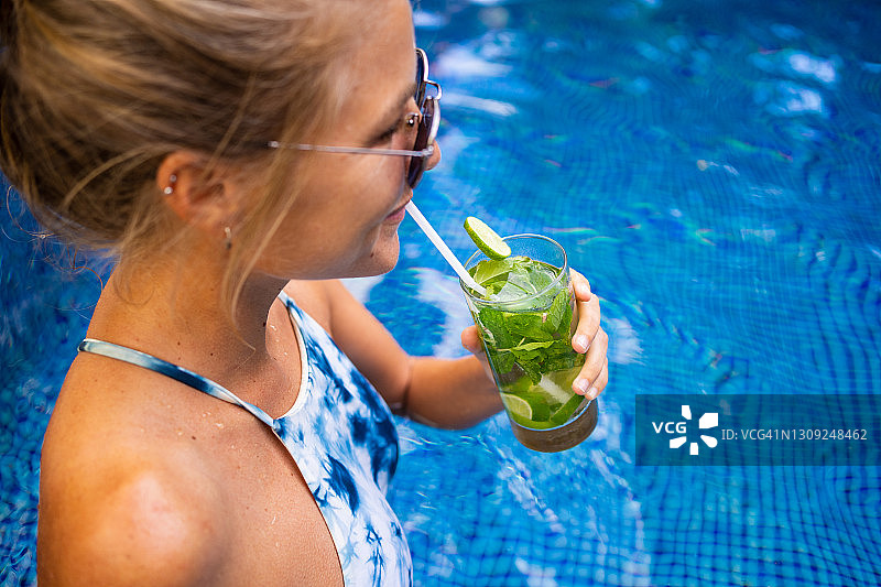 聚焦在游泳池边戴墨镜的金发女人手中的一杯饮品图片素材