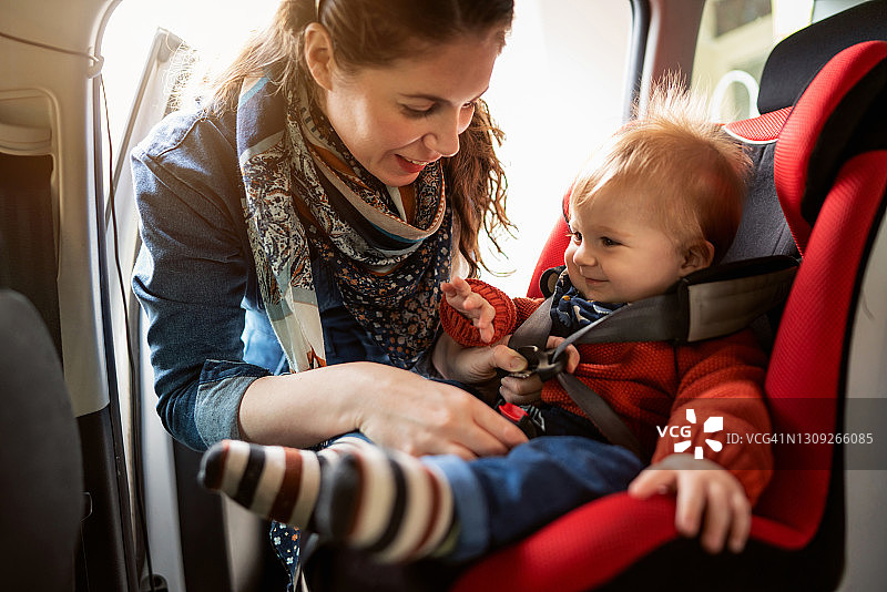 微笑的母亲将男婴放入汽车座椅并系好安全带图片素材