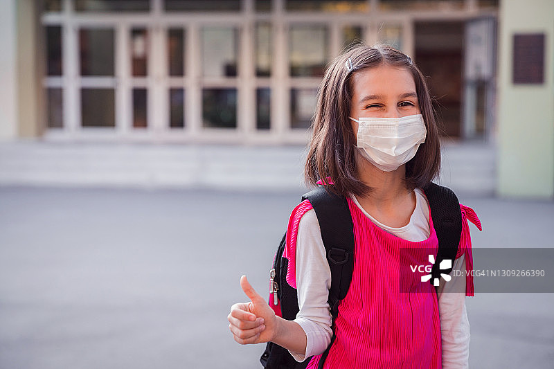 戴防护口罩并竖起大拇指的快乐女孩图片素材
