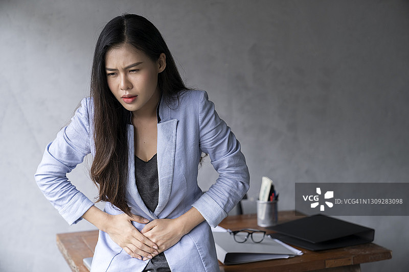 在办公室里胃痛的年轻亚洲女商人图片素材