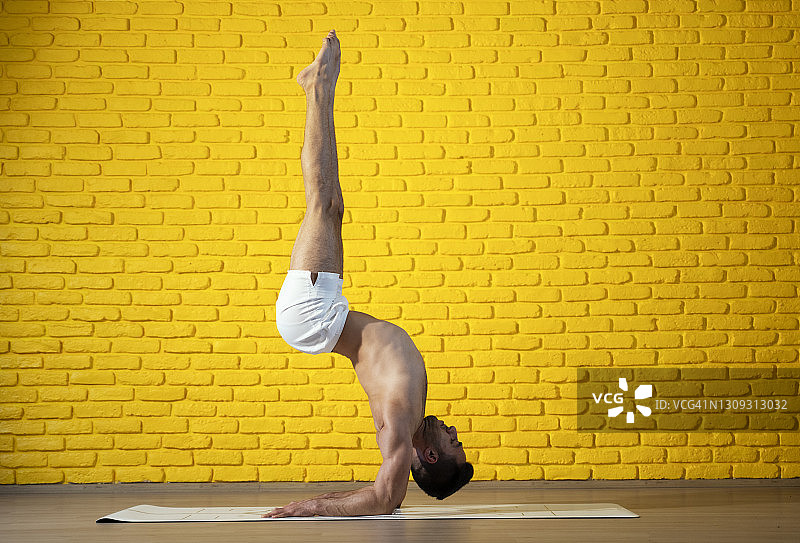 年轻的健壮男人在健身房做瑜伽倒立图片素材