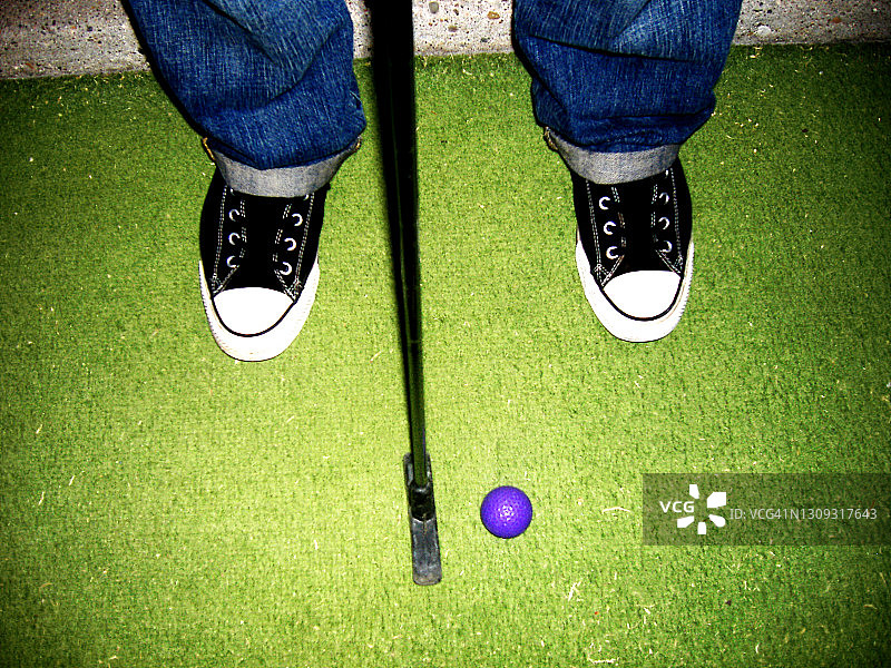 穿着卷起牛仔裤和运动鞋的酷家伙，卷边牛仔裤，玩迷你高尔夫图片素材