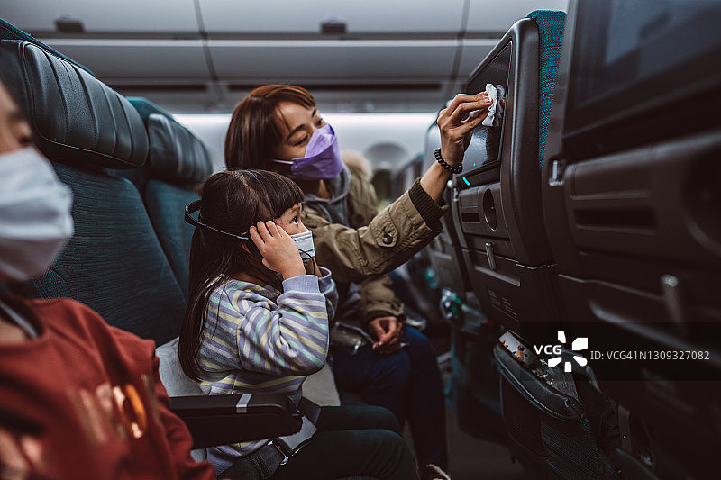 乘坐飞机时，戴着防护口罩的母女用消毒湿巾清洁座椅靠背电视屏幕图片素材