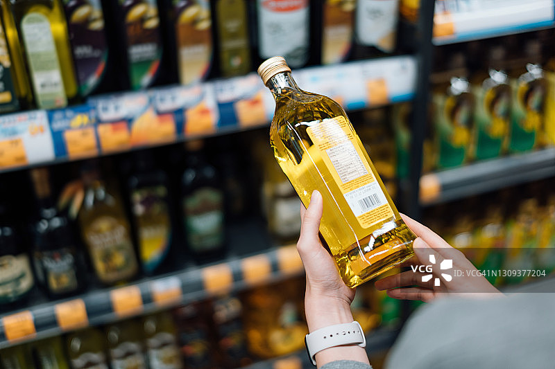 年轻女子在超市购物的特写。站在过道旁，拿着一瓶有机食用油，阅读营养标签并检查背面的成分图片素材