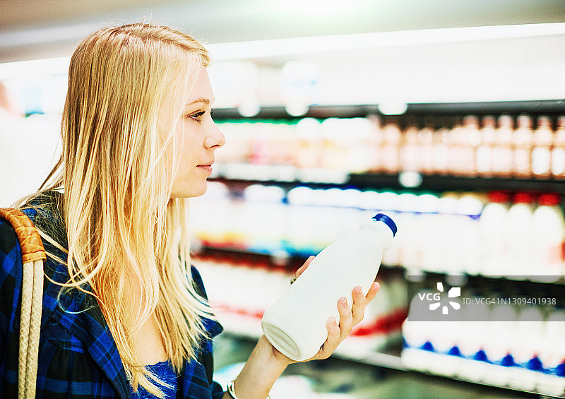 在超市乳制品区选择牛奶的年轻金发女子图片素材