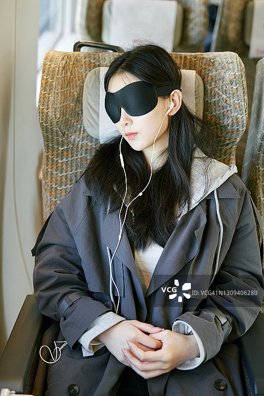 戴着眼罩在火车上听音乐的年轻亚洲女孩图片素材