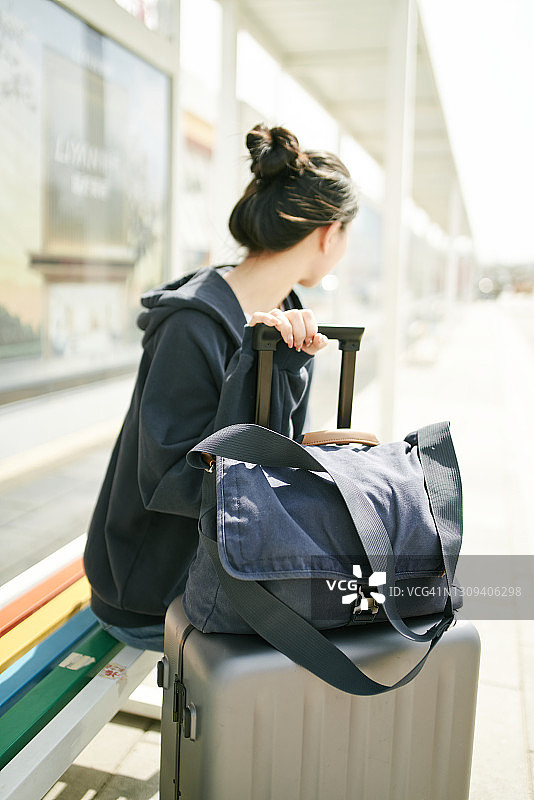 年轻的亚洲女孩带着行李箱在路边等公交车图片素材