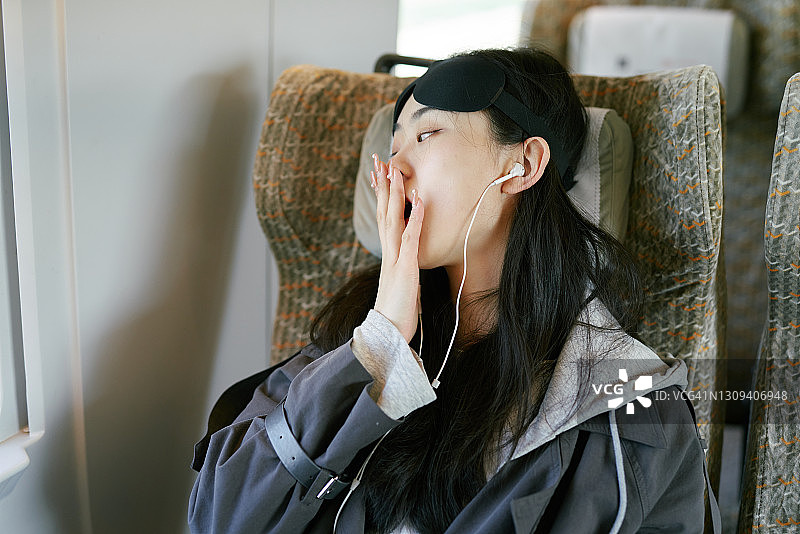 戴着眼罩在火车上听音乐的年轻亚洲女孩图片素材
