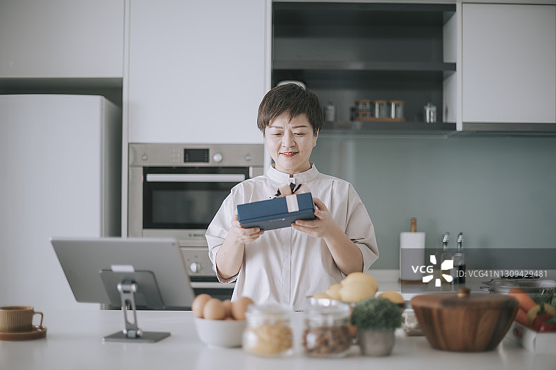 中国中年妇女在厨房柜台上接收并打开礼物图片素材