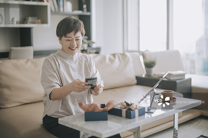 亚洲中年女人在客厅接受并打开礼物图片素材