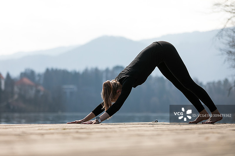 瑜伽老师在平静的湖边演示下犬式图片素材