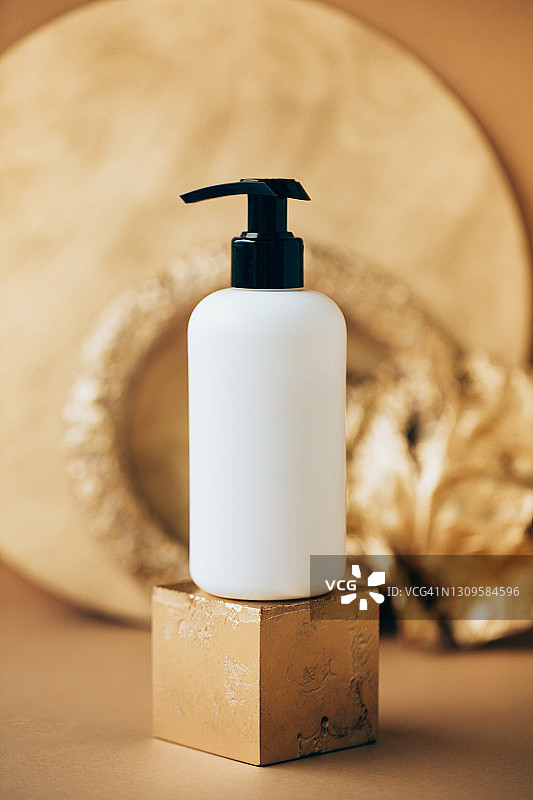 带分配器的白色塑料瓶放置在金色装饰品附近的立方体形状的讲台上。天然化妆品概念正面视图图片素材