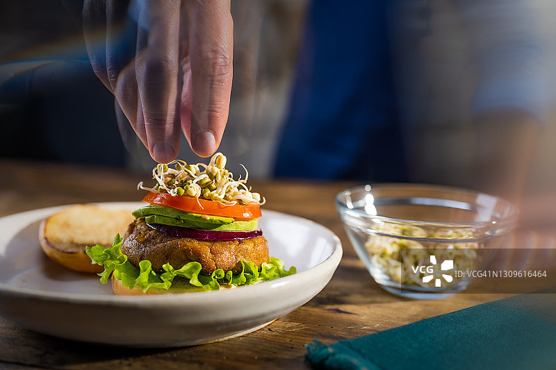 在厨房准备汉堡，添加食材，包括发芽的绿豆、新鲜蔬菜和纯素汉堡图片素材