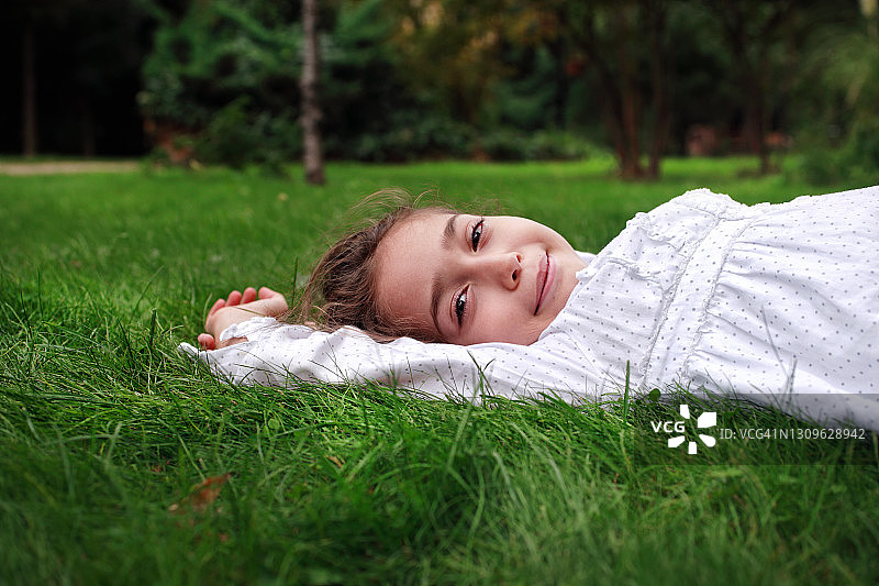 快乐小女孩躺在绿草上的肖像图片素材