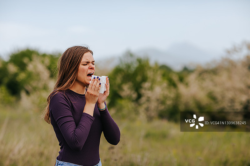 在户外因过敏症状而擤鼻子的女人图片素材