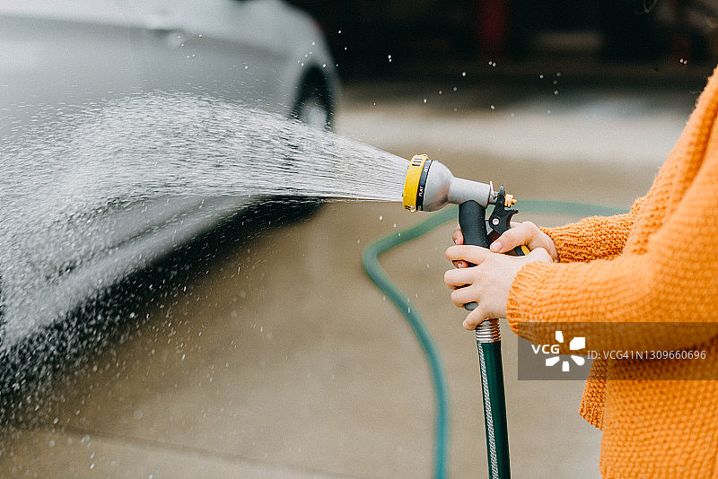 小女孩手持软管冲洗汽车图片素材
