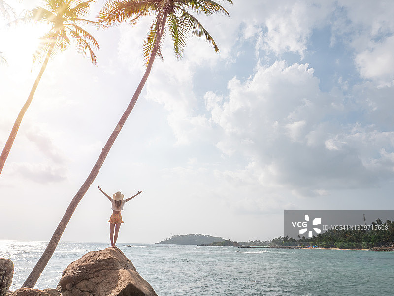 年轻女人在海边岩石上伸展双臂图片素材
