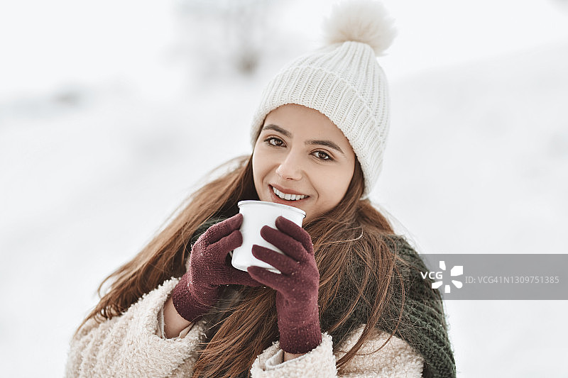 戴着针织帽在雪山上享受热咖啡的微笑女性图片素材