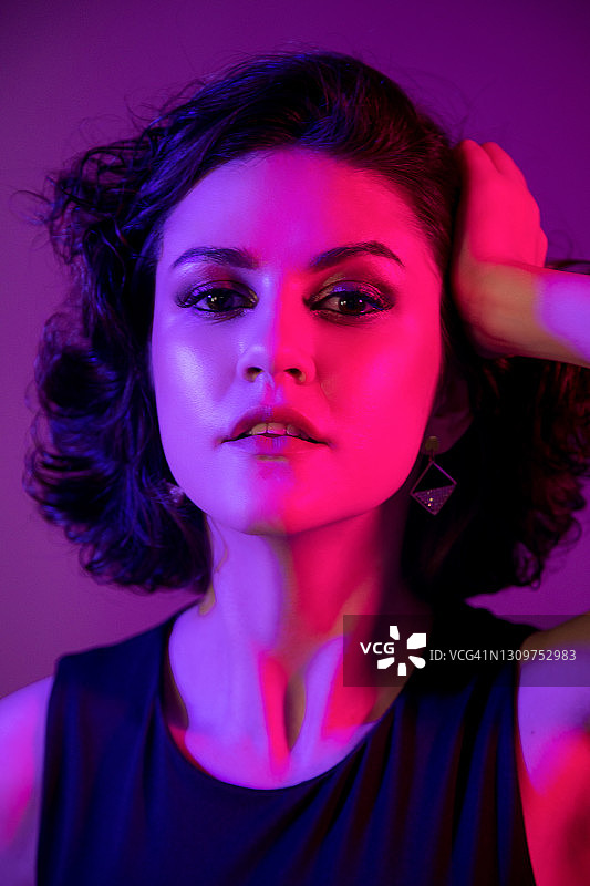 在蓝色和粉色灯光下的照相馆里，留着黑色波波头的年轻女孩特写肖像图片素材