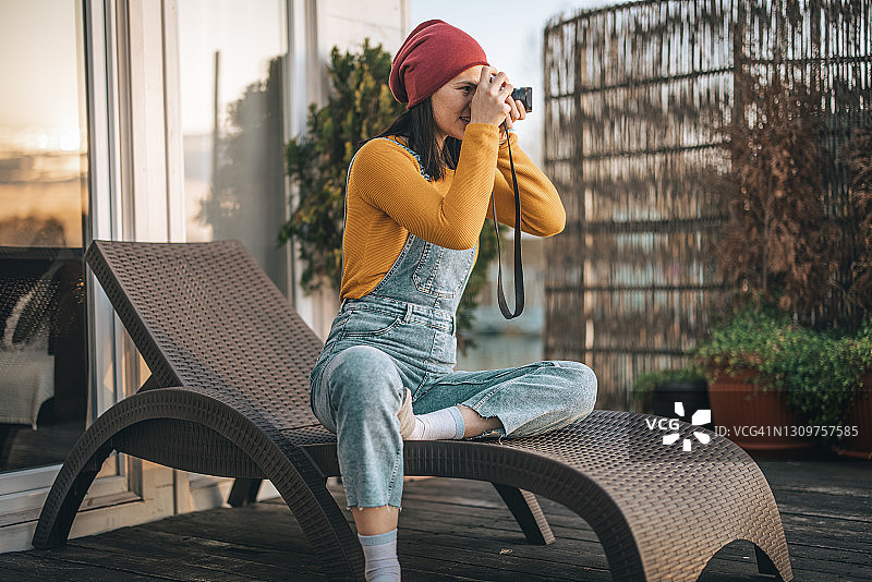 女人坐在阳台躺椅上用相机拍照图片素材