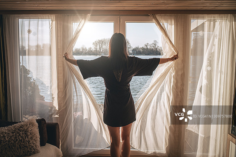 身穿浴袍的女子打开窗帘向外看图片素材