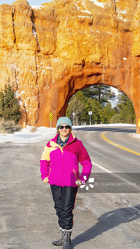 女人在美国犹他州12号公路的红色石拱门前摆姿势，通往布莱斯峡谷图片素材