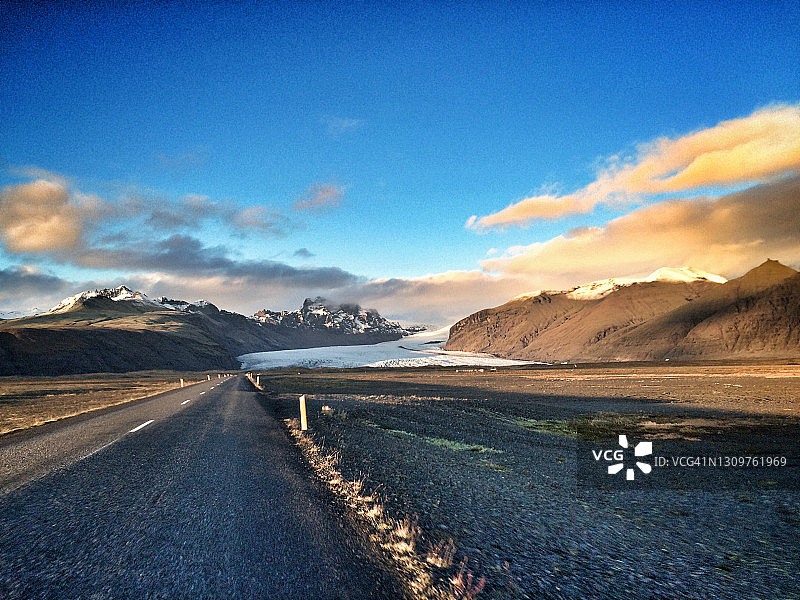 冰岛乡村日落时分的笔直公路，背景是冰川和山脉图片素材