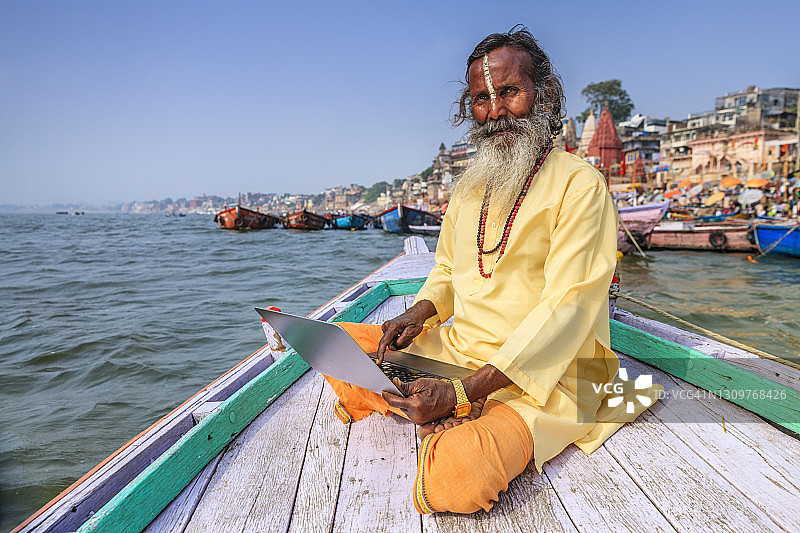 瓦拉纳西，在恒河圣河的船上使用笔记本电脑的印度圣人图片素材