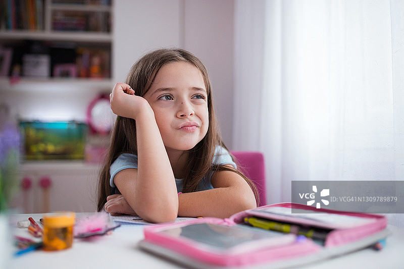手握铅笔趴在桌子上思考学校的女学生图片素材