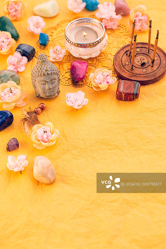 精神之春俯视图：石英治疗石与鲜花、佛头雕像和黄色皱纹纸上的香，以及复制空间图片素材