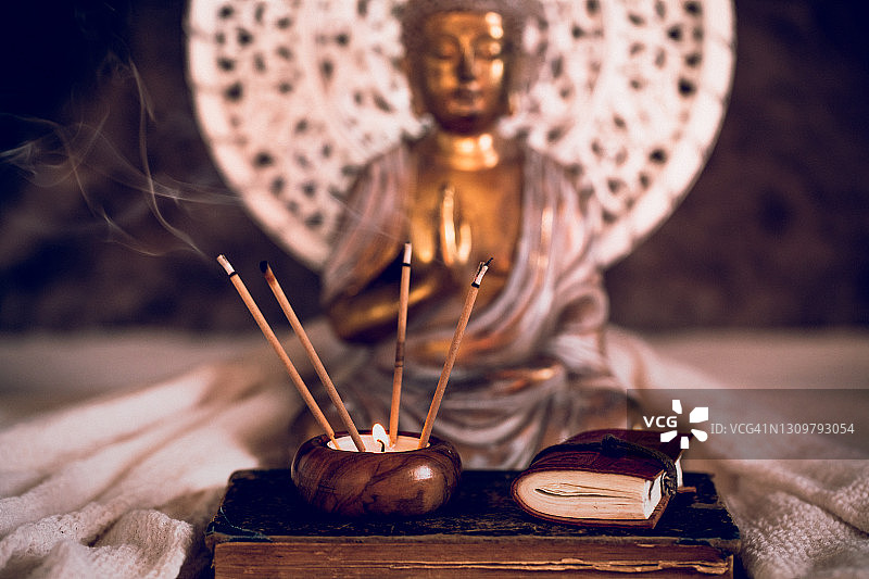 金色佛像前，旧书上一支点燃的香和带日记的蜡烛图片素材