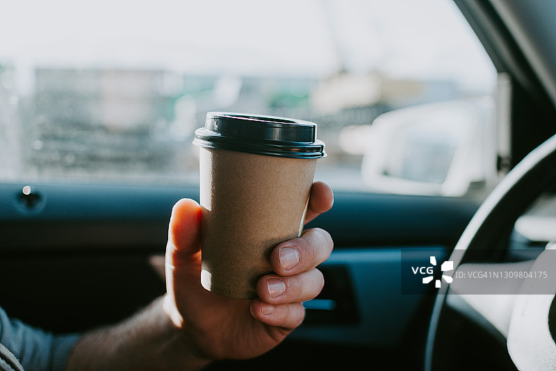男人在车内手持咖啡，一次性餐具，行驶中路上的咖啡饮品图片素材
