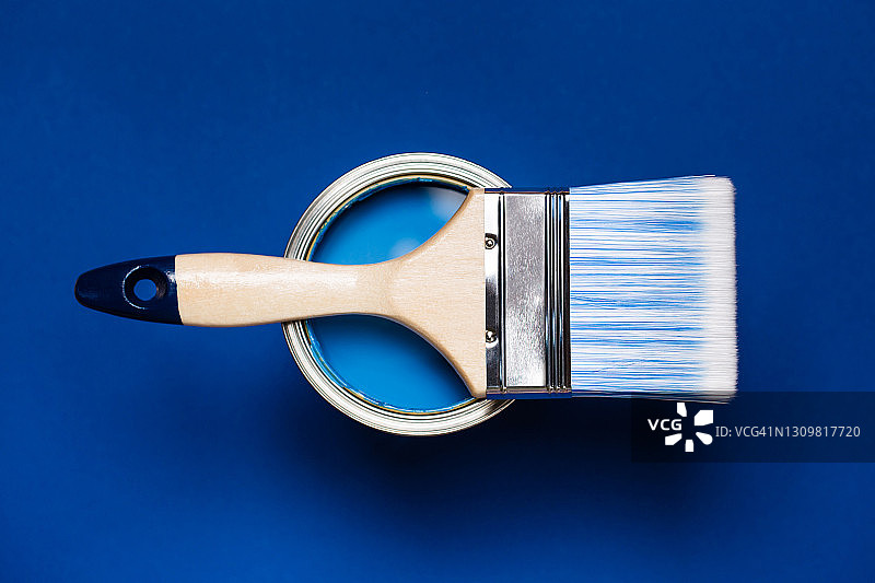 清洁油漆刷在金属桶与蓝色油漆翻新工程在明亮的蓝色背景。平的风格。为您的设计复制空间。家居室内重新装修的概念。颜色样本的设计理念图片素材