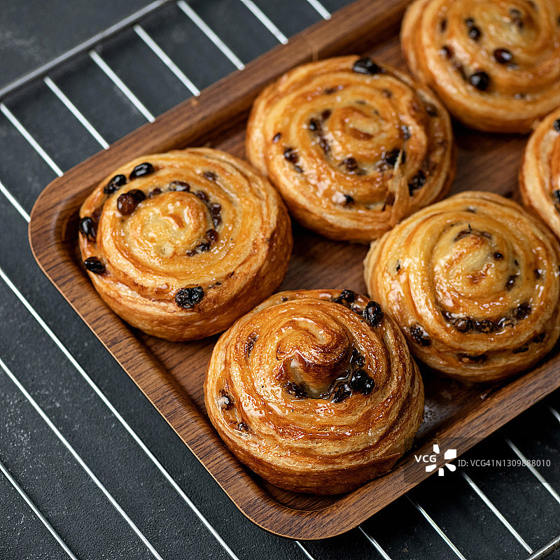 肉桂葡萄干酥皮卷：新鲜出炉的托盘甜点，柔和焦点图片素材